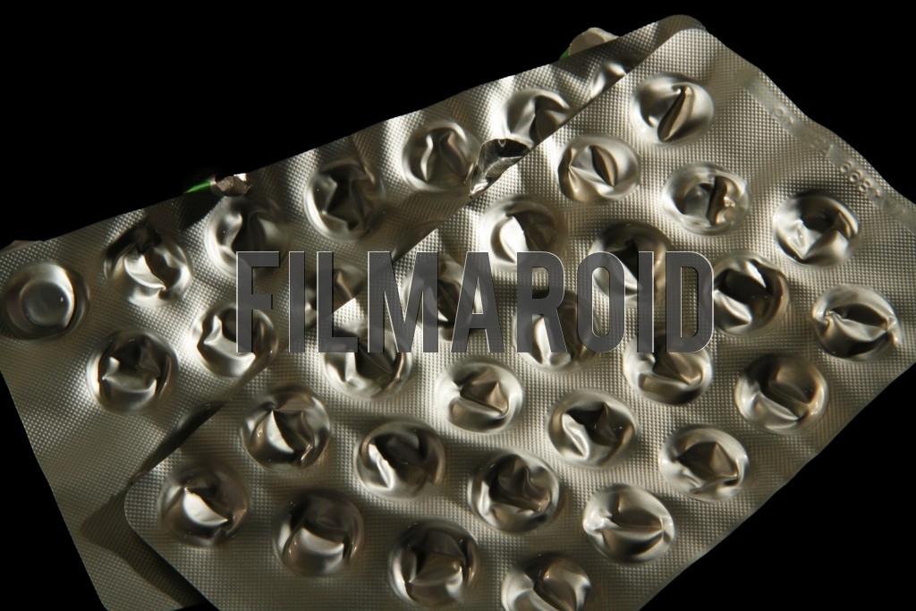Closeup of an empty pack of pills - Detail shot of an isolated pair of empty shiny aluminum packs of pills against a pitch black background
