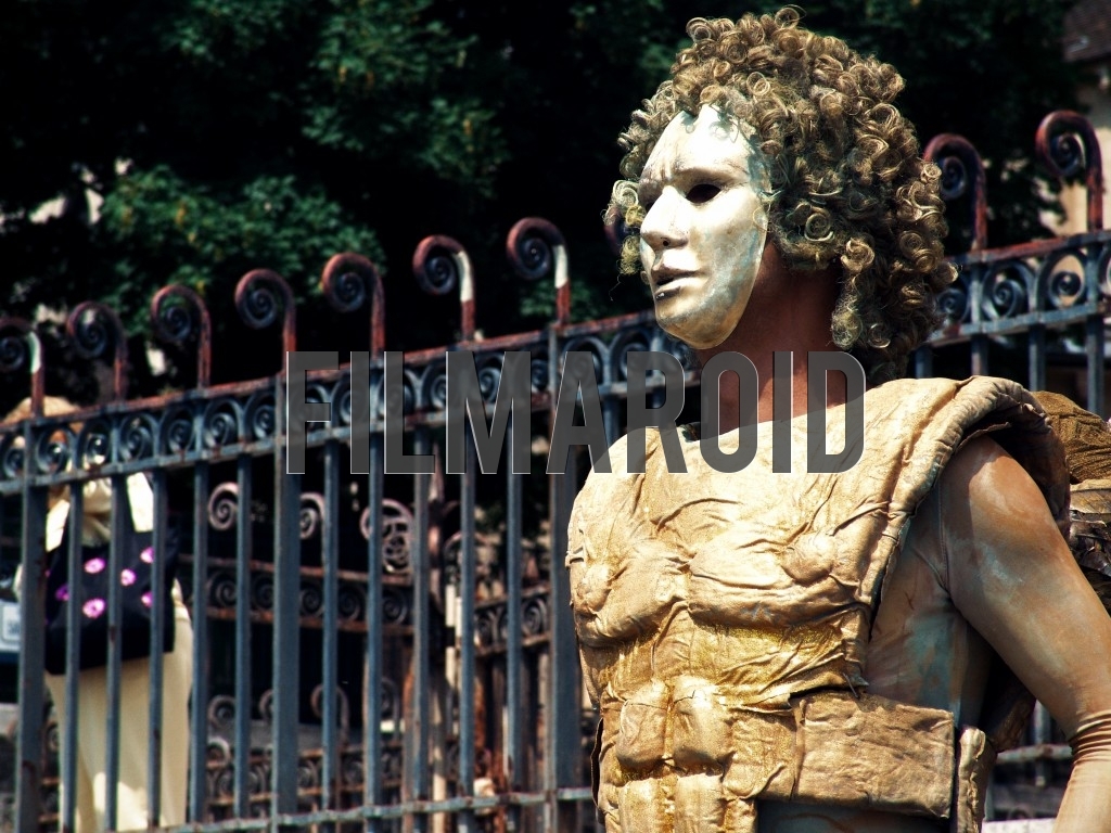 A street artist from the city of Paris France wearing an elaborate golden costume and a wig and white mask