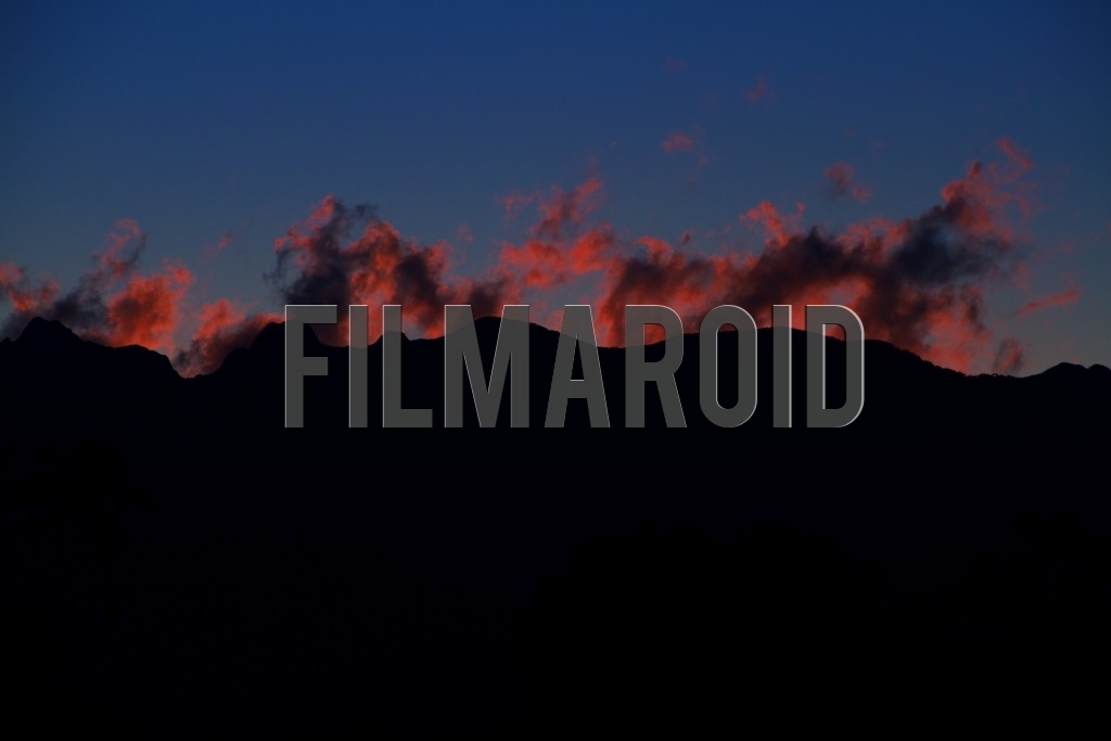 Beautiful afternoon view of the Andean mountain range silhouette with red fire like clouds against blue sky background